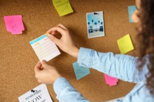 Hands pinning a weekly planner to a bulletin board with notes and photos