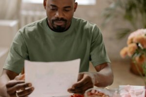Man sitting at a table, reading a printed letter with a thoughtful expression