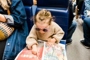 Child in sunglasses reading a newspaper while riding public transit