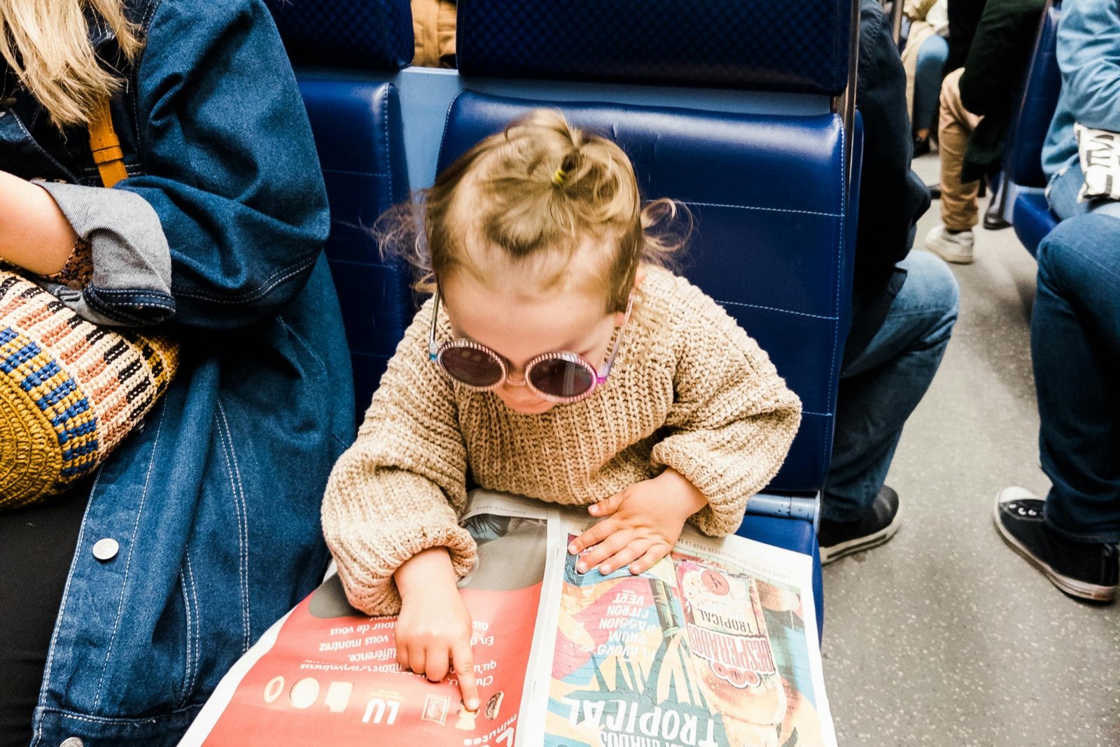Child in sunglasses reading a newspaper while riding public transit