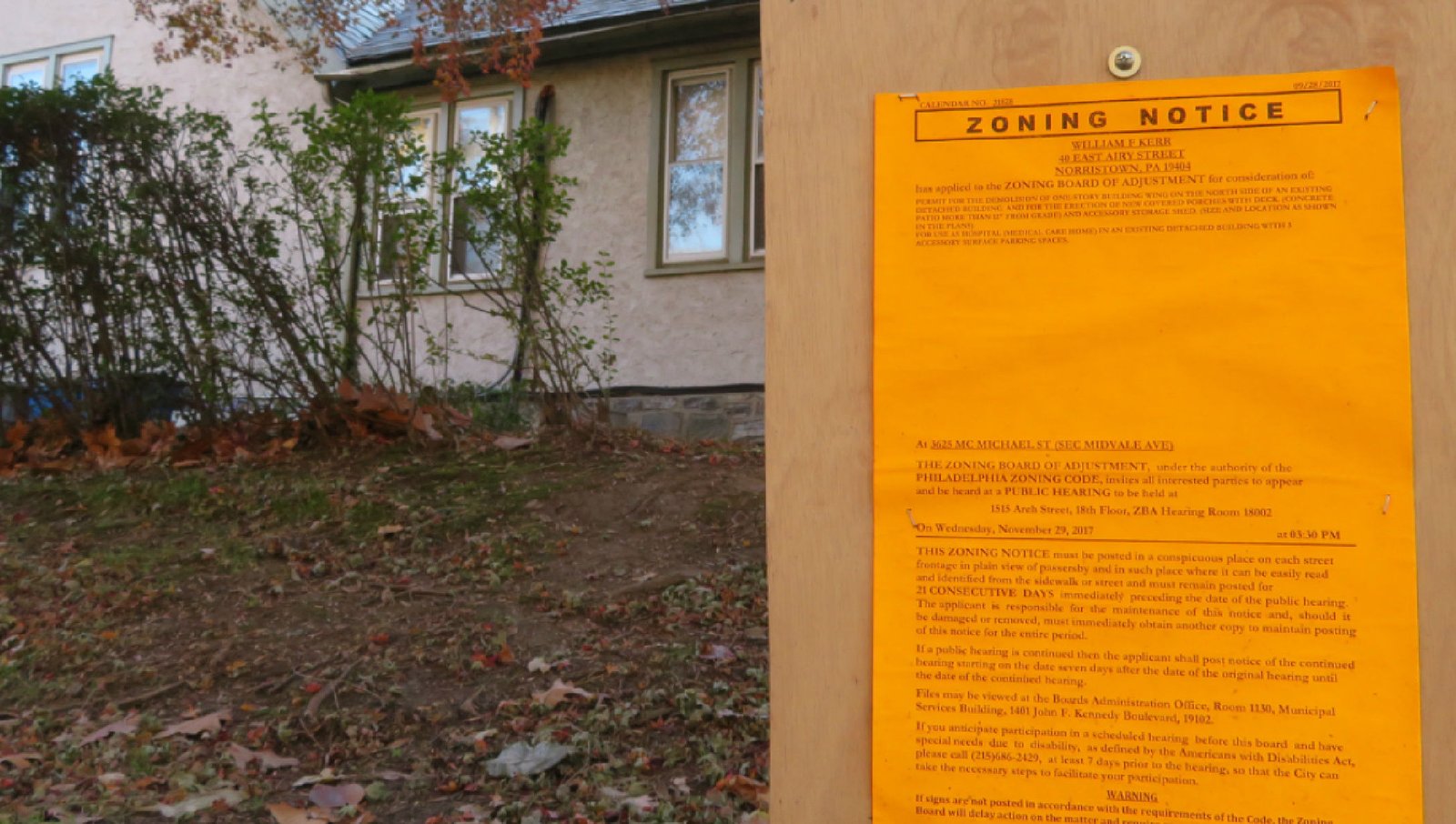 A bright orange zoning notice posted on a wooden board outside a residential building.