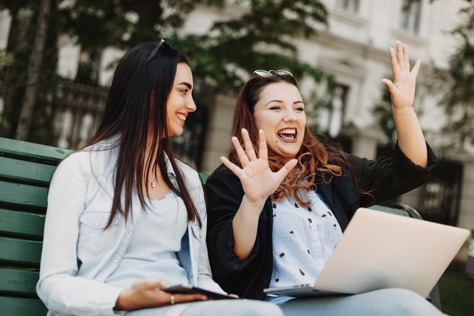Two women talking and laughing outdoors with a laptop, representing local storytelling for nonprofits through community connection